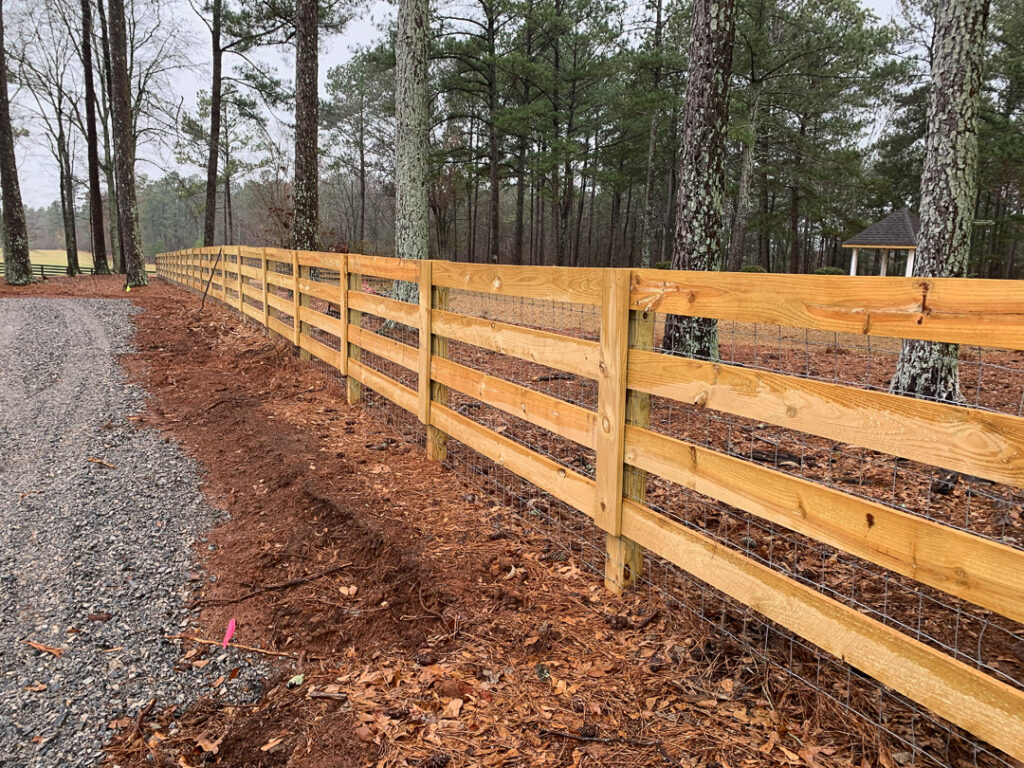 Four-rail wood farm fence along a gravel driveway
